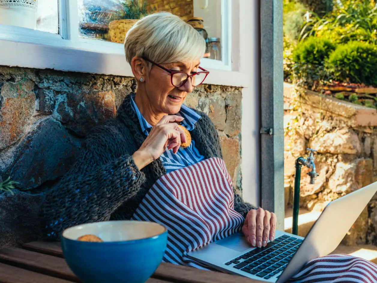 An elderly person lounging outside their home, using a laptop.