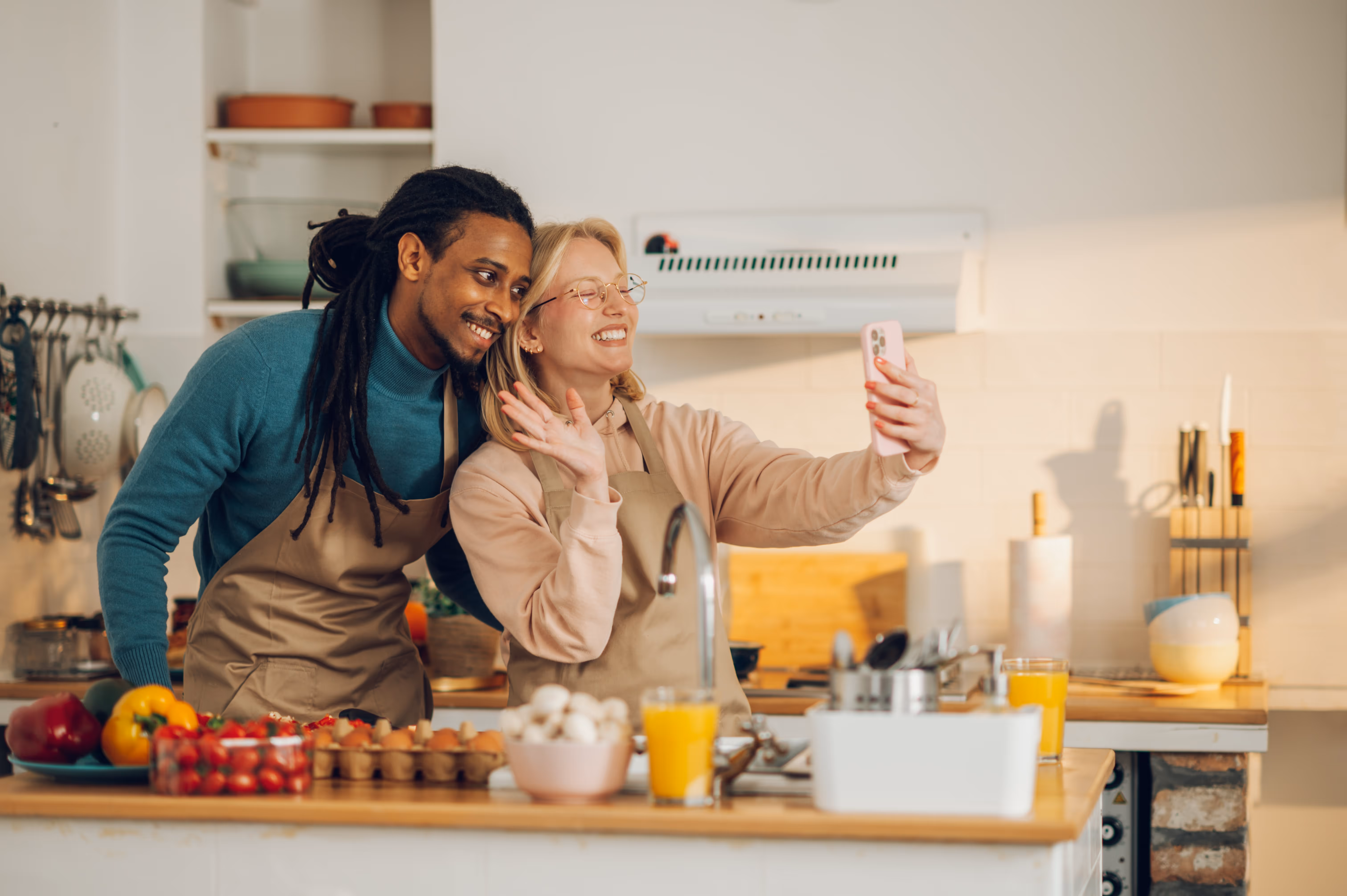 A man and woman smiling while taking a selfie together in a bright kitchen.