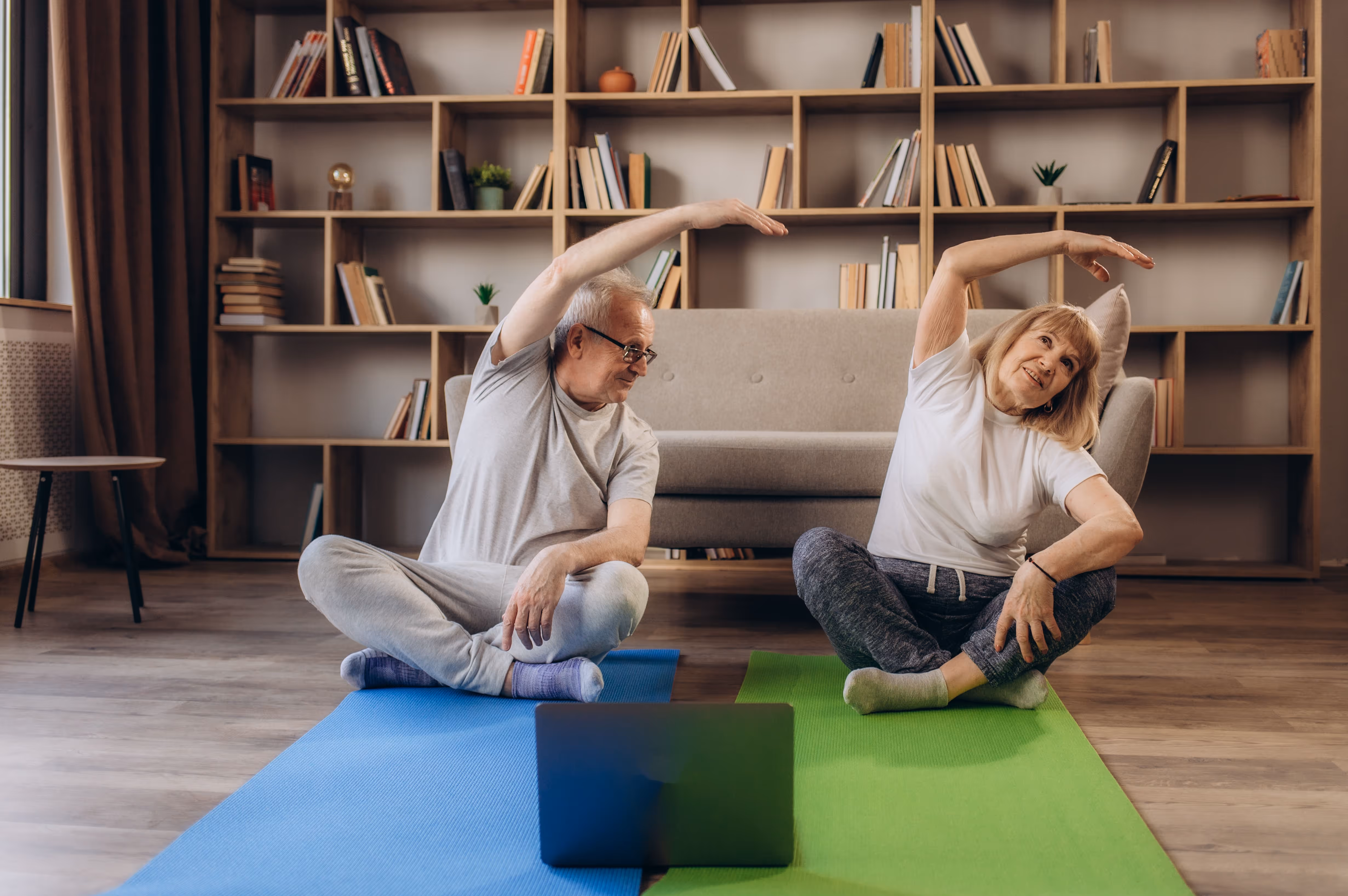 An older couple practicing yoga together in front of a laptop, focusing on their poses and maintaining balance.